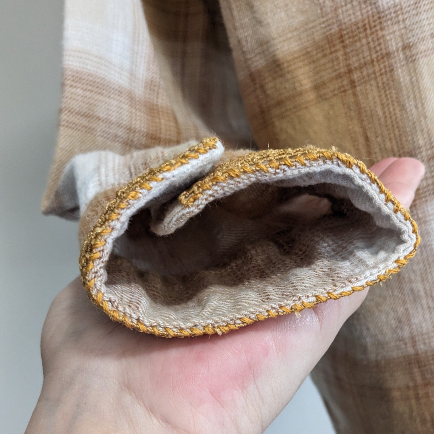 Hand holding a beige fabric with gold trim against a neutral background